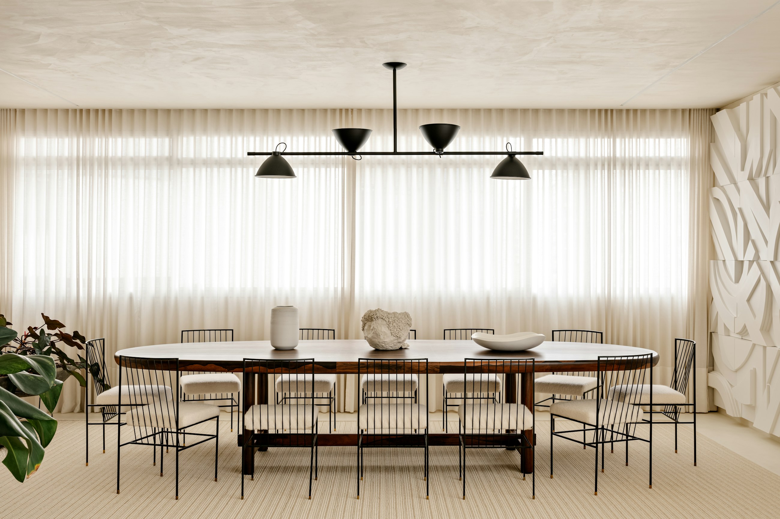 Dining room with a rosewood oval table, wire chairs, and sheer curtains, furnished with Brazilian modernist design