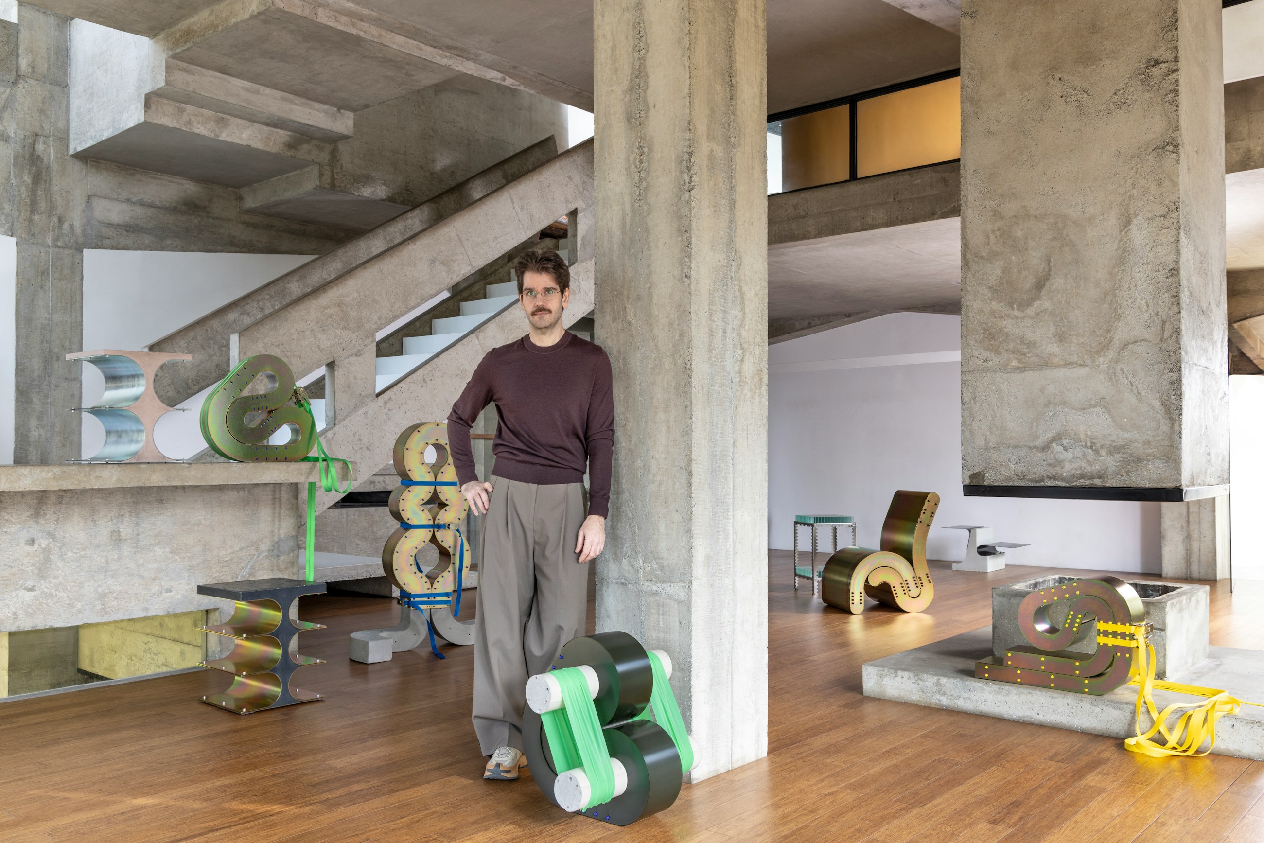 Artist Lucas Simões with his sculptural furniture in a concrete modernist interior